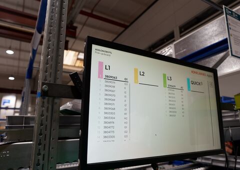 Demagin CTO-kokoonpanoalue, jossa Agilon-virtahyllyn näyttö näyttää jonossa olevat tilaukset. Työasema tukee pick-to-light-ohjattua keräilyä, jossa operaattorit kokoavat nostolaitesarjat visuaalisten ohjeiden avulla SAP Fiori -integraation ja Agilon-varastoautomaation materiaalivirran tukemana kohti lopullista kokoonpanoa.